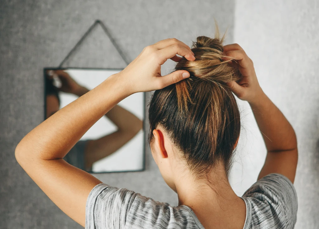 Woman putting hair in a bun while looking in the mirror